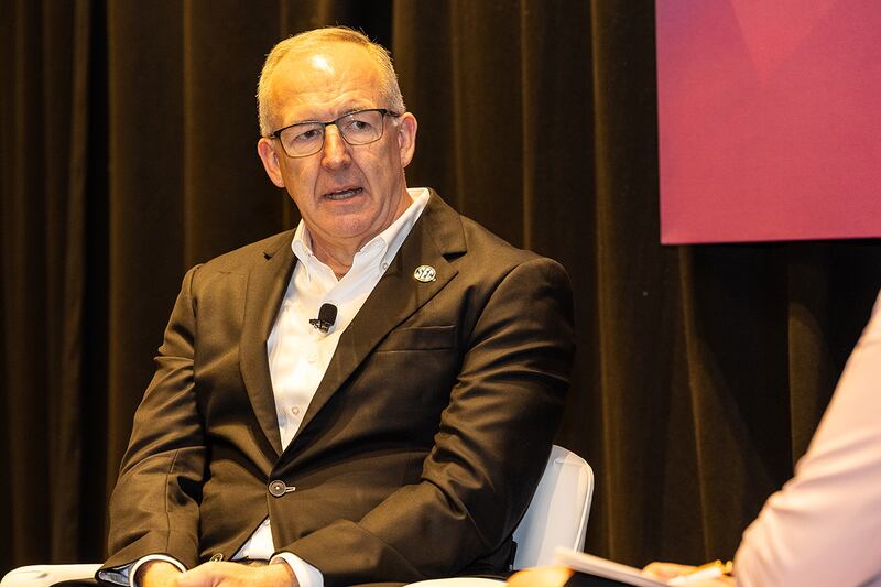 A man with graying hair and glasses in a brown jacket, white shirt and light brown pants with an SEC button, Greg Sankey.