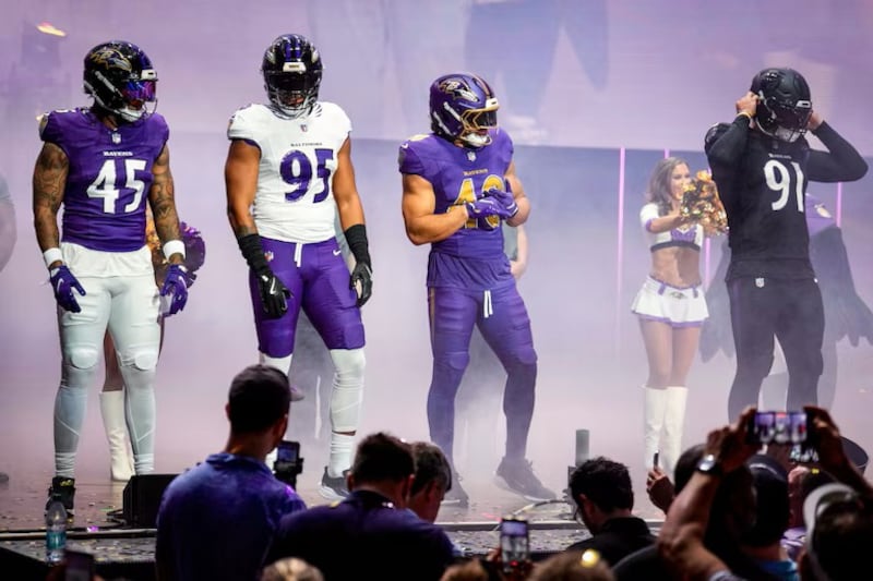 Ravens players model new uniforms on stage with cheerleaders behind them.