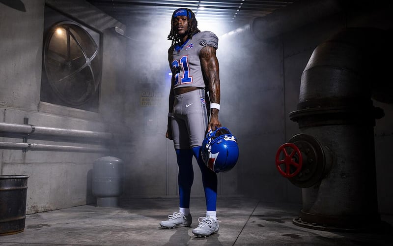 A Bills player poses in a grey Bills uniform, holding a blue helmet.